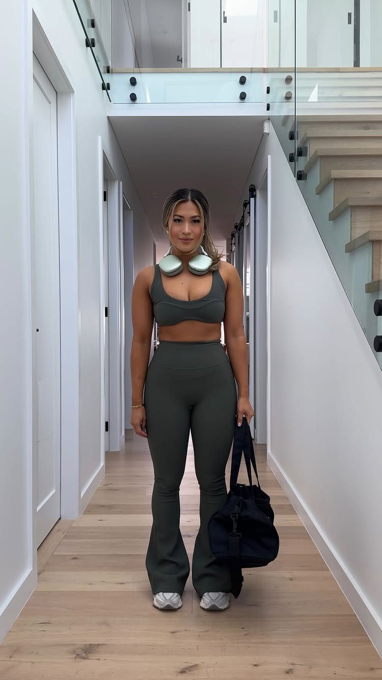 Woman in olive green athleisure set with headphones and gym bag in hallway