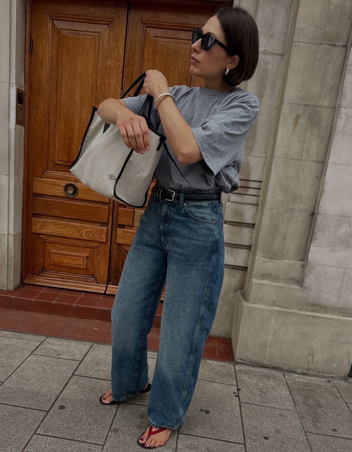Woman wearing high-waisted blue wide-leg jeans and a grey top standing outdoors.