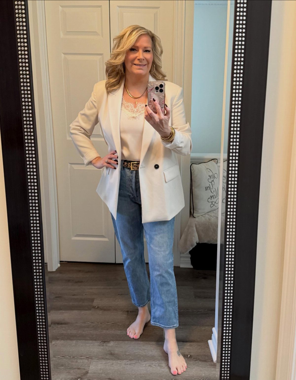 Woman wearing a white fitted blazer and light blue jeans in a mirror selfie