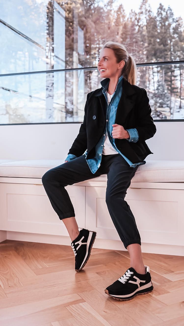 Woman wearing a black blazer, blue shirt, and black trousers sitting on a bench.