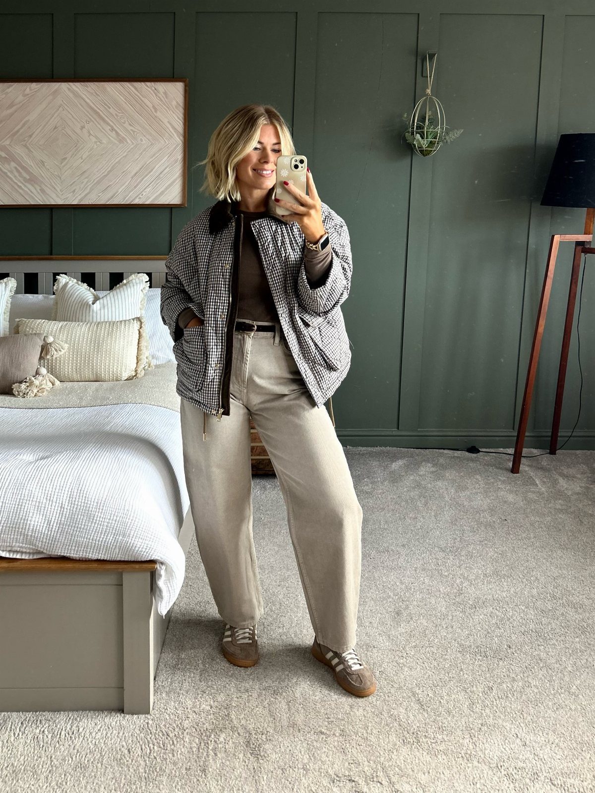 Woman wearing a patterned jacket over a brown top and beige trousers.