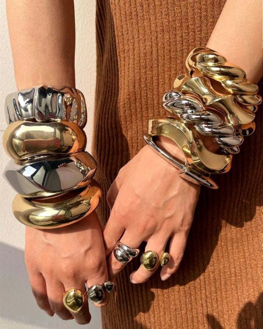 Chunky gold and silver metallic bangles and rings on a person's hands.