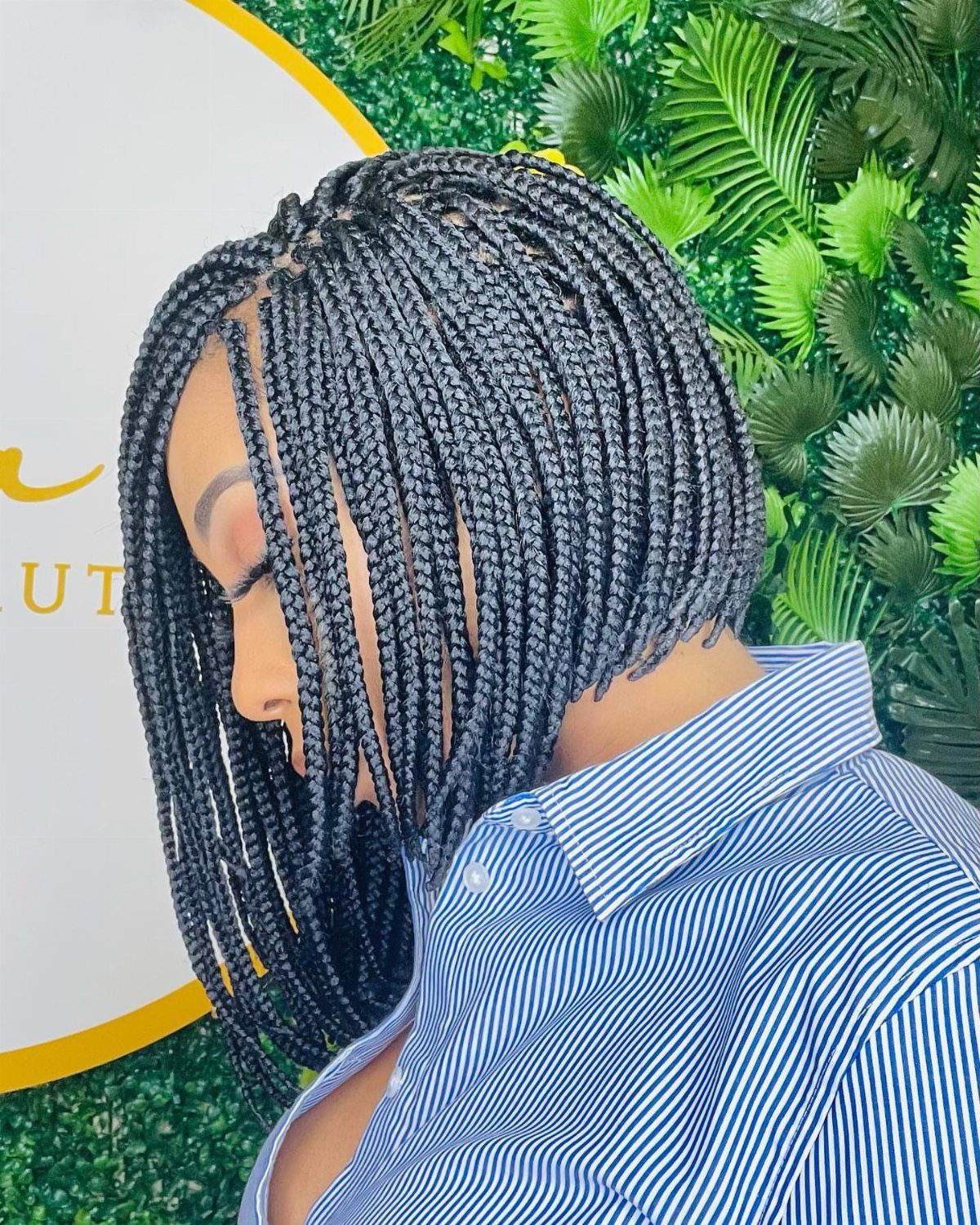 Woman with a chin-length black braided bob hairstyle wearing a striped blue shirt.