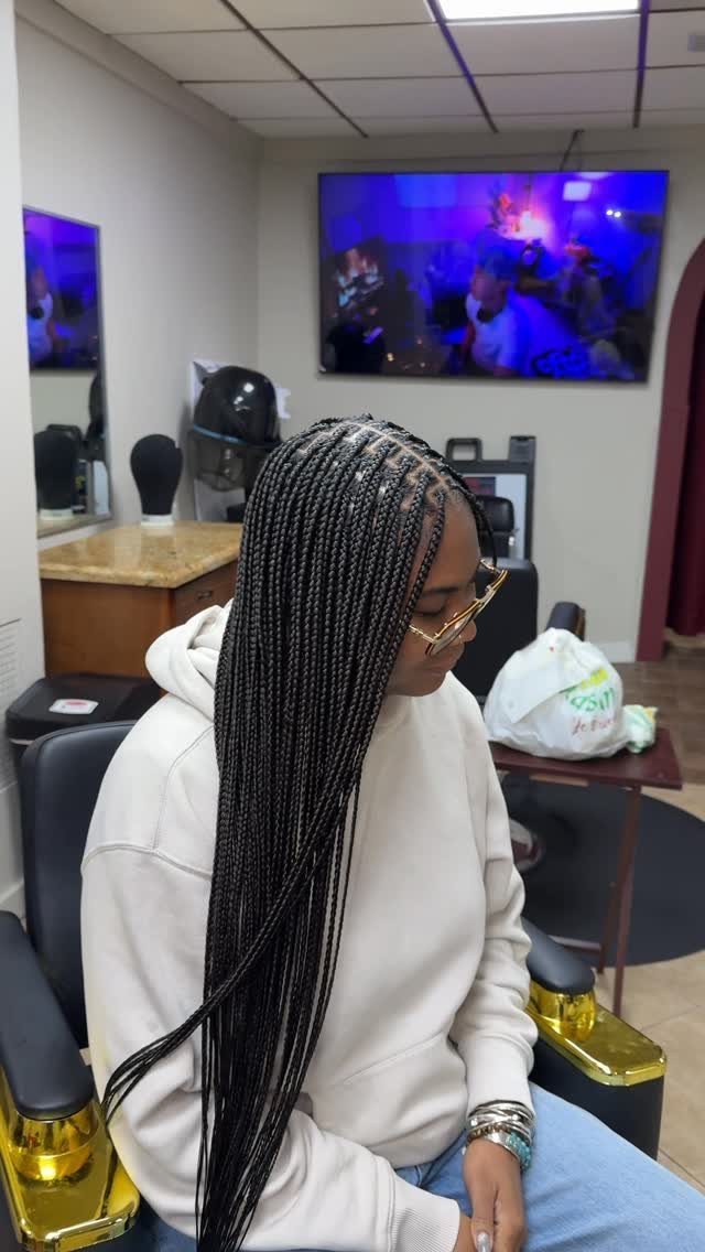 Woman with long, thin black micro braids wearing a white hoodie in a salon