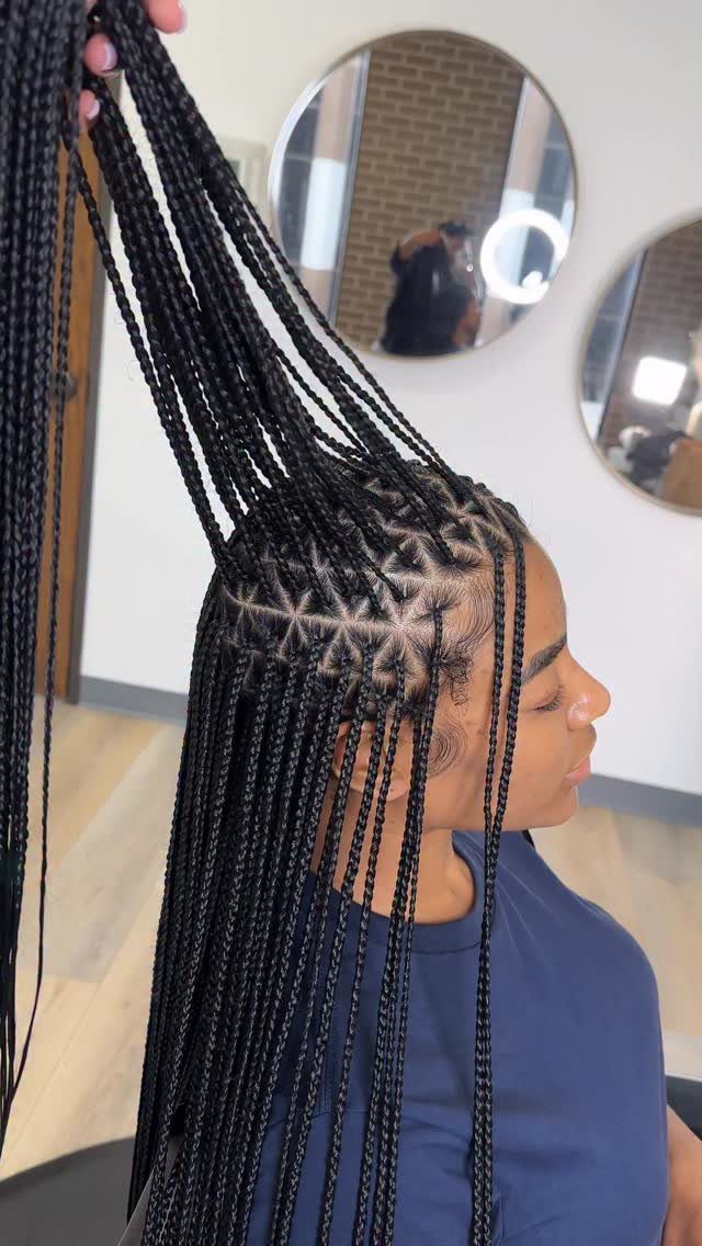 Woman with long black box braids featuring triangle-shaped scalp parts in a salon.