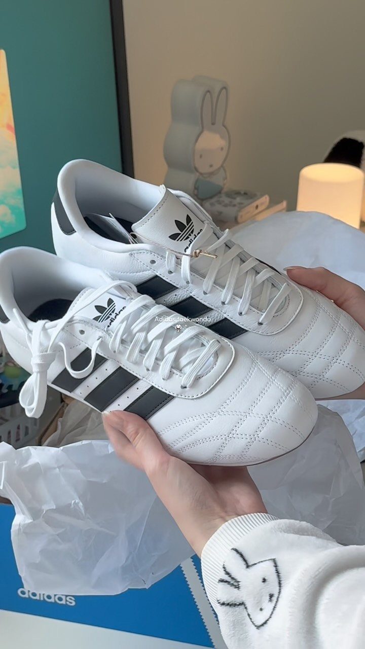 White leather Adidas sneakers with black stripes and white laces held by hands.