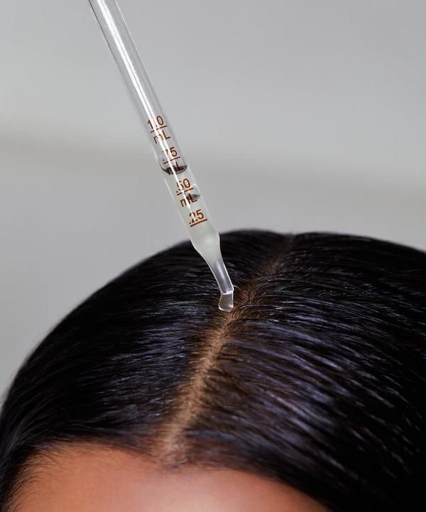 Glass dropper applying clear liquid to the scalp of thick dark hair