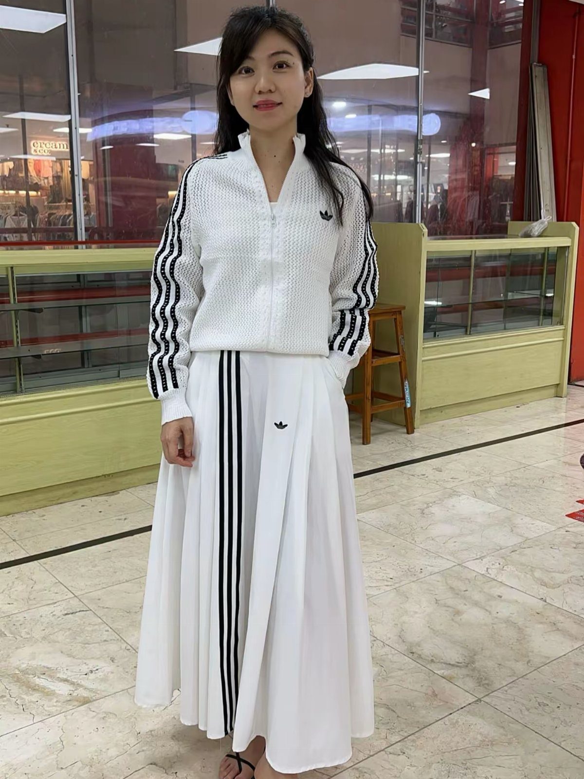 Woman wearing a white athletic zip-up jacket and matching white maxi skirt.