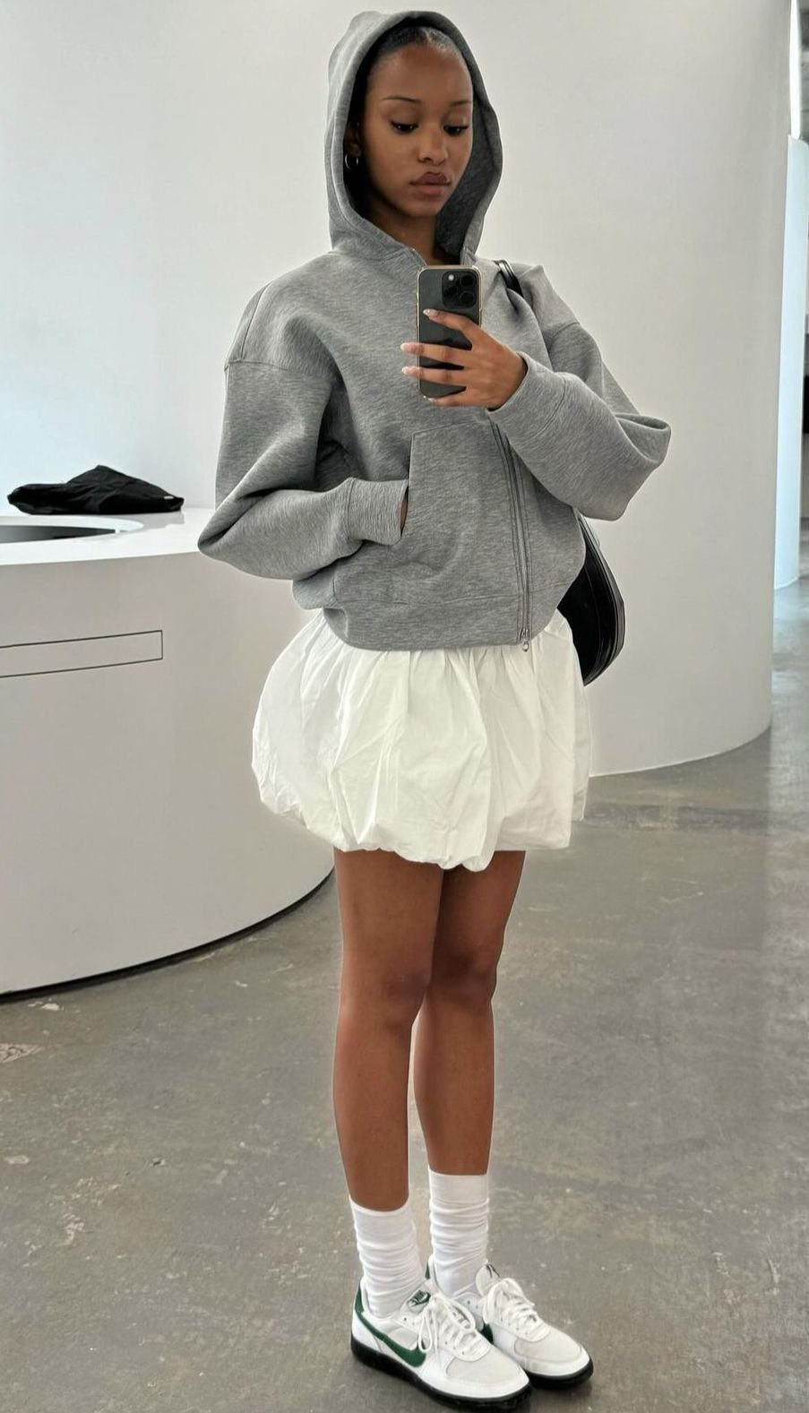 Woman wearing a grey hoodie and white ruffled mini skirt with white sneakers.