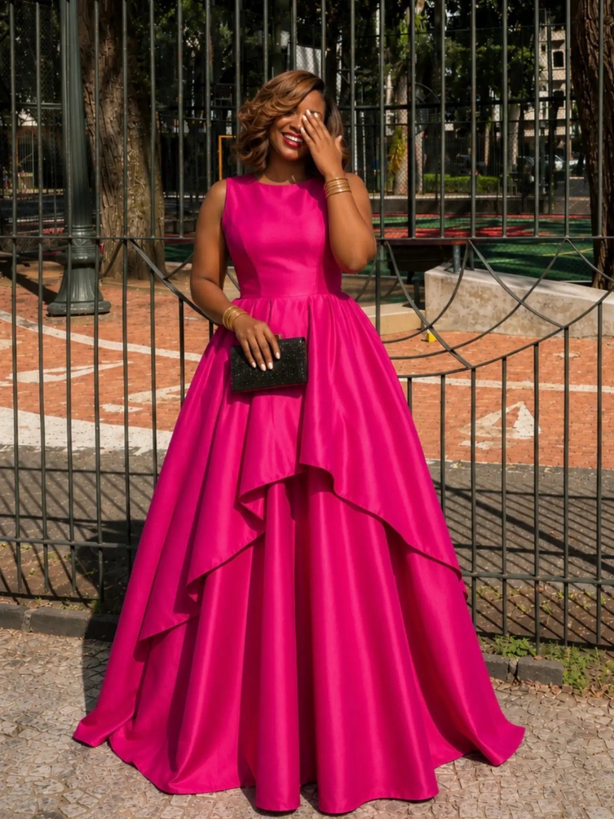 Woman in a bright pink floor-length satin gown holding a black clutch bag.