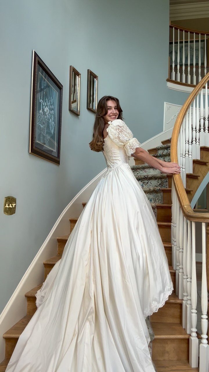 Woman in a voluminous cream vintage wedding dress standing on a wooden staircase