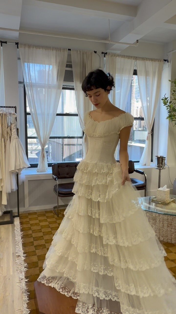 Woman wearing a cream vintage wedding dress with tiered lace skirt in a studio