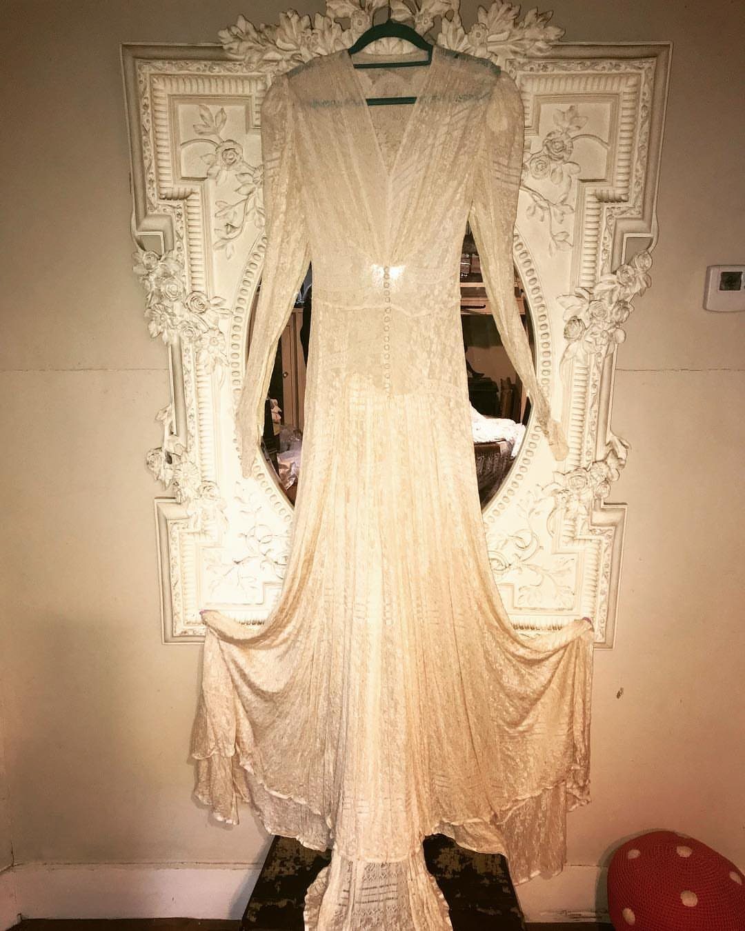 Cream vintage wedding dress with lace hanging before an ornate white mirror