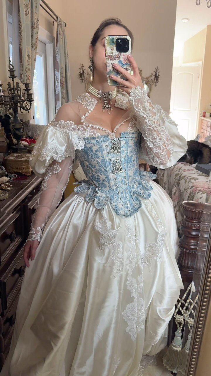 Woman in a vintage white and blue lace wedding gown taking a mirror selfie.