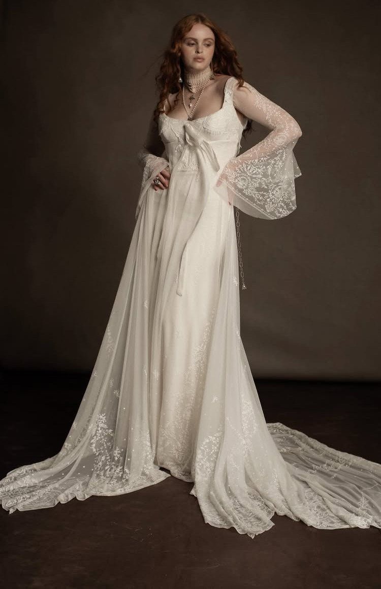 Woman wearing a flowy white vintage wedding dress with lace sleeves and train.