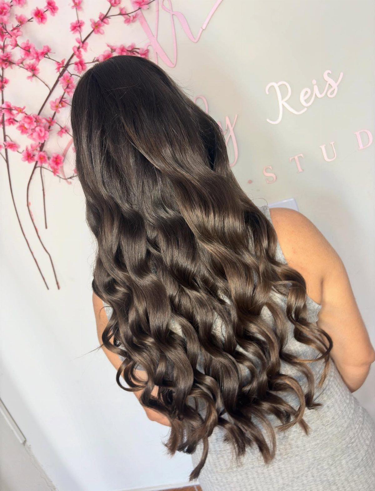 Long dark brown hair styled in voluminous, glossy bouncy waves from behind.