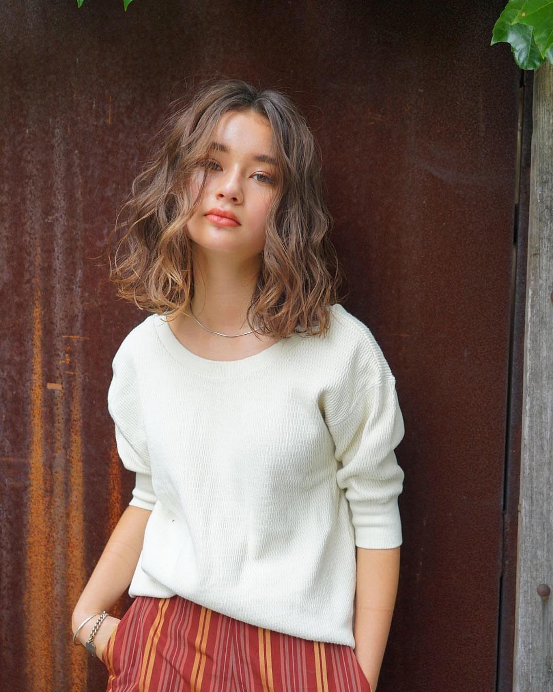 Woman with a wavy lob hairstyle wearing a white top and striped pants.