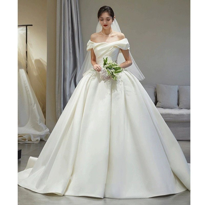Wedding Dresses Off White: 9 Ideas for Every Bride 6 Woman in an off-white off-the-shoulder ballgown wedding dress holding a white flower bouquet.