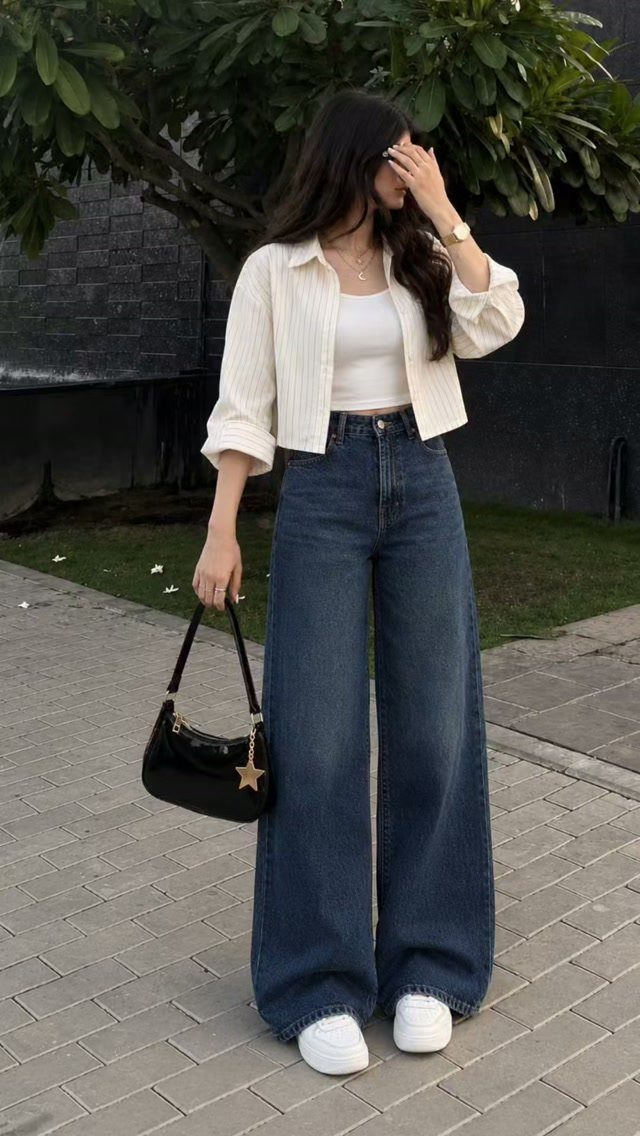 Woman in open white shirt and wide-leg blue jeans holding a black handbag