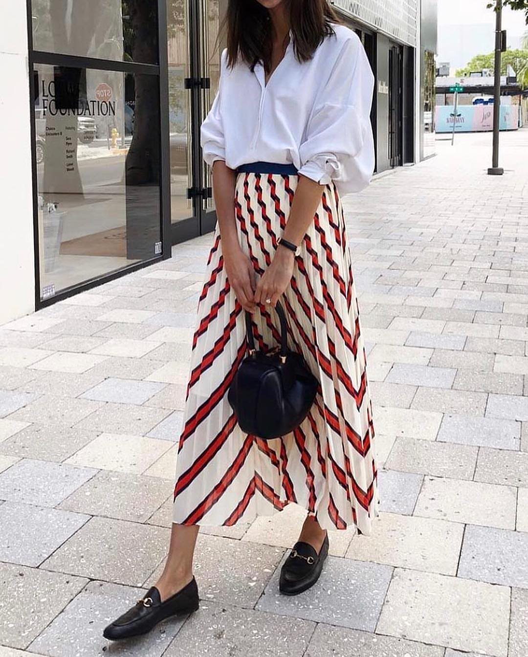 Person wearing a white button-down shirt and a striped pleated midi skirt.