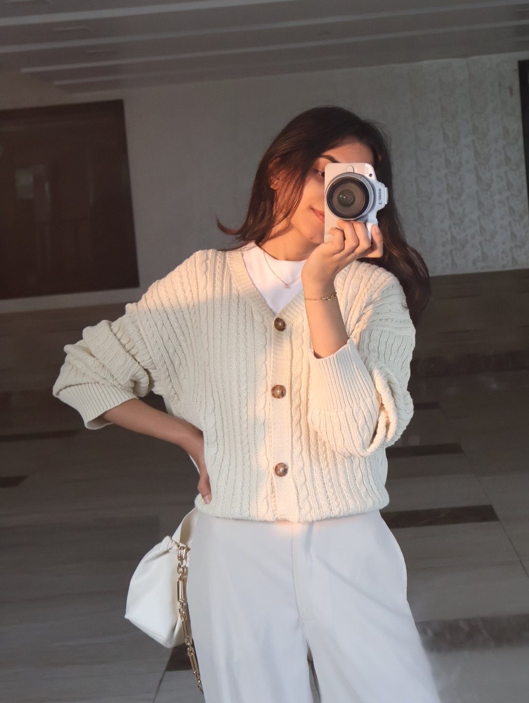 13 Winter Wear Ideas for Women: Coats, Knits and Boots 13 Woman in a cream cable knit cardigan and white pants taking a mirror selfie