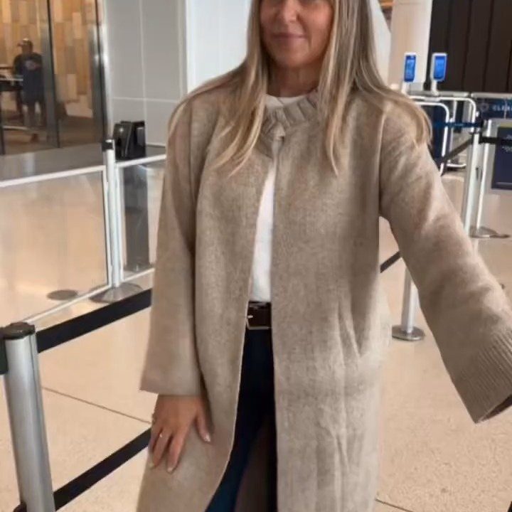 13 Winter Wear Ideas for Women: Coats, Knits and Boots 7 Woman wearing a long beige duster coat and dark jeans in a terminal.