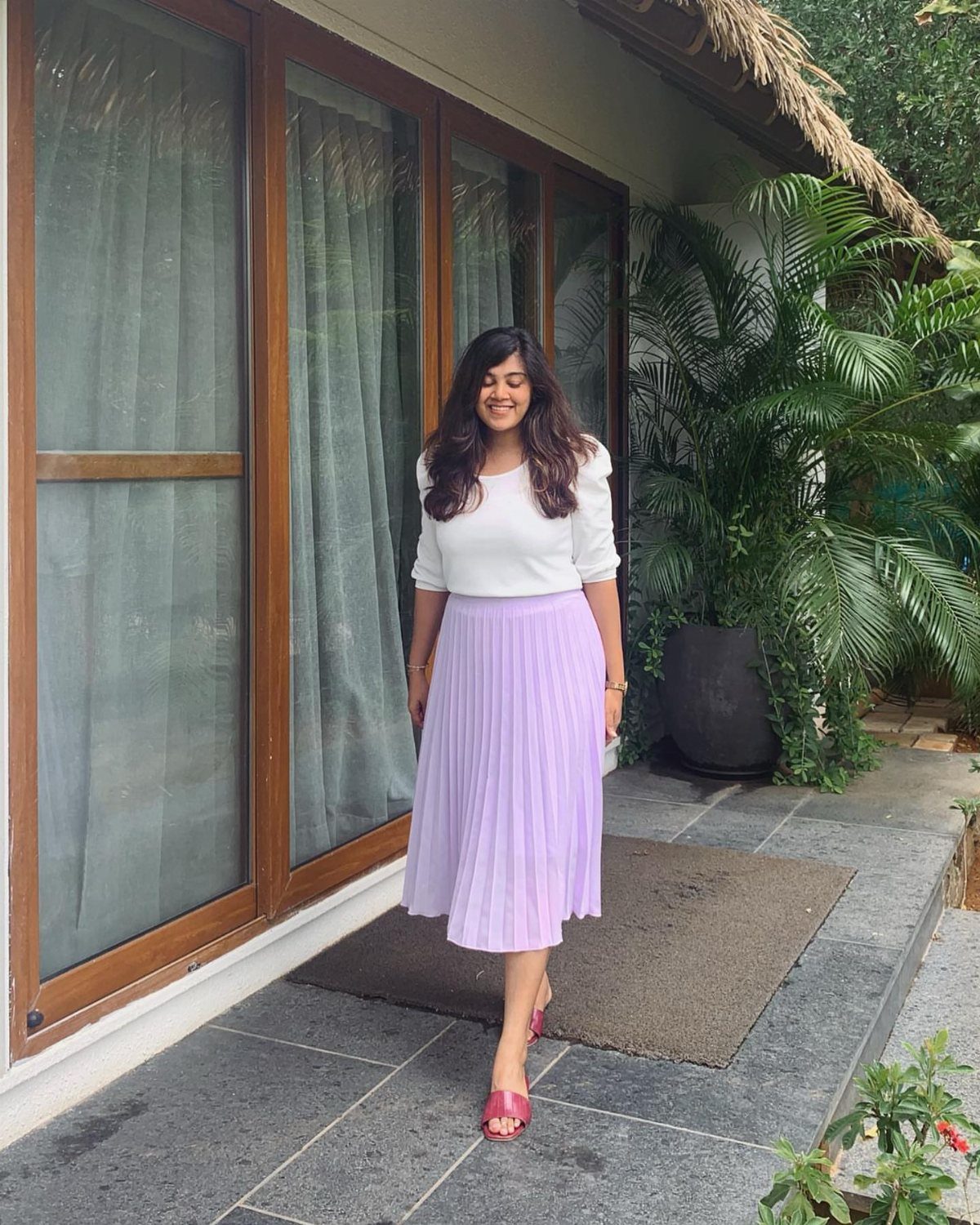 14 Women Skirt Outfits for Every Season and Occasion 4 Woman wearing a white blouse and lavender pleated midi skirt standing on a porch