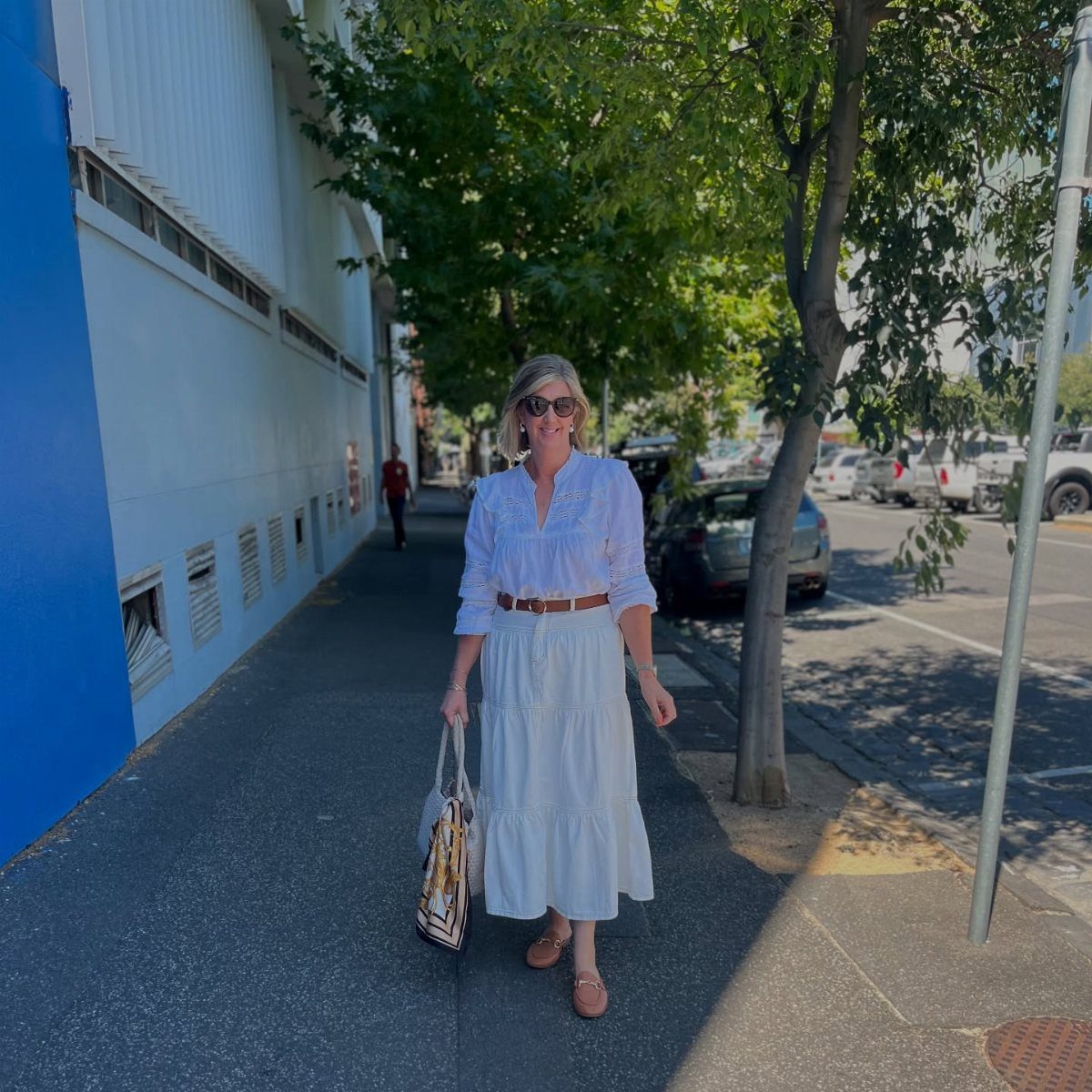 14 Women Skirt Outfits for Every Season and Occasion 11 Woman in white blouse and white midi skirt walking on a city sidewalk