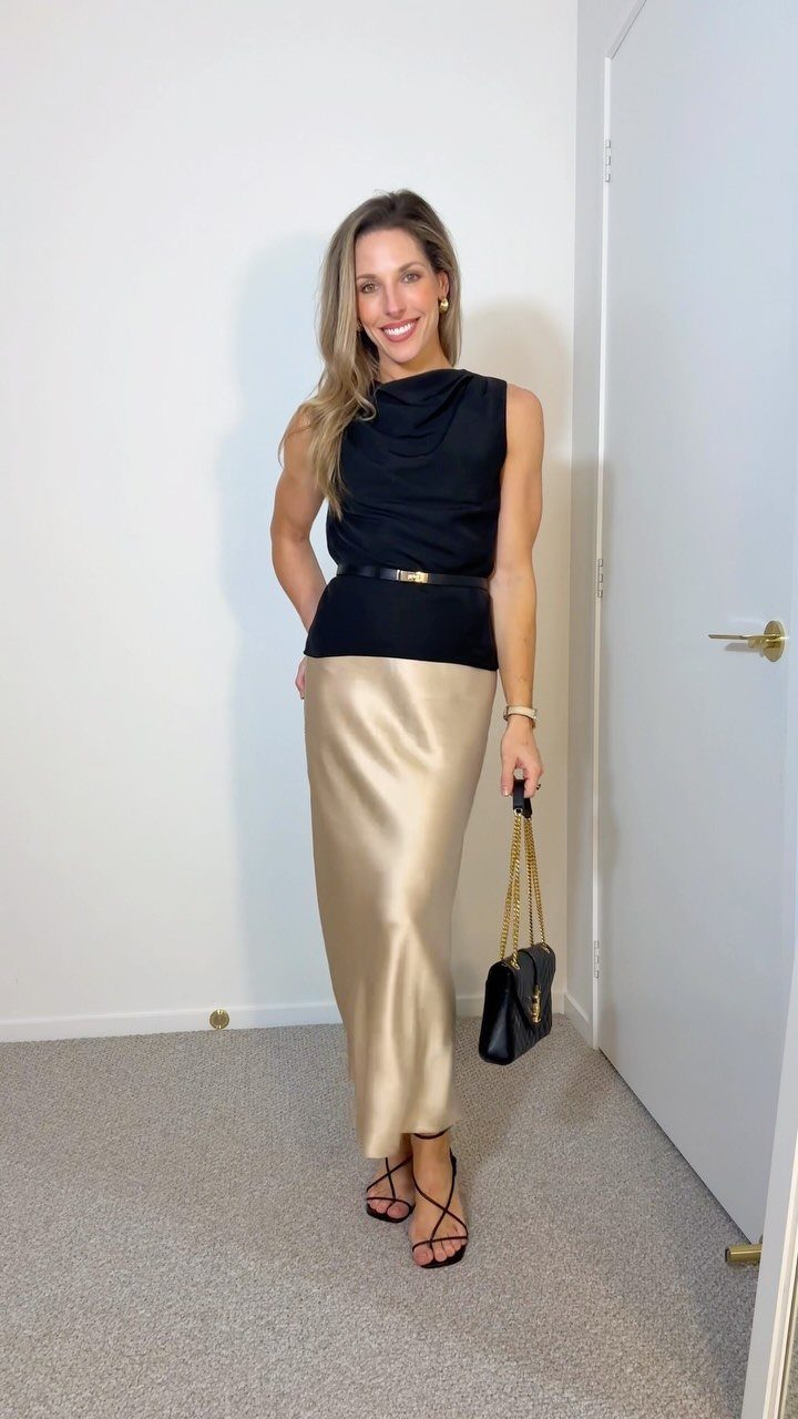 14 Women Skirt Outfits for Every Season and Occasion 8 Woman wearing a champagne satin slip skirt and black sleeveless top with handbag.